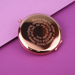 Rose gold compact mirror with personalised spiral message engraved on the front, shown in close up shot on purple background.